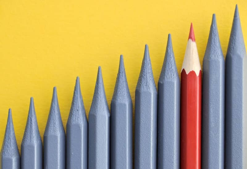 Ein roter Stift, der unter einer Reihe von grauen Stiften heraussticht.