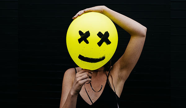 Eine Person hält einen gelben Luftballon mit einem Smiley-Gesicht vor ihr Gesicht.