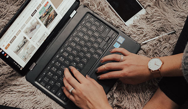 Eine Person schreibt auf einem Bett sitzend einen Blog auf einem Laptop.