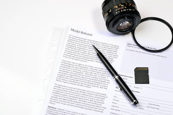 Neben einem Kameraobjektiv liegen eine Speicherkarte, ein Stift und eine Einverständniserklärung mit der Überschrift Model Release.