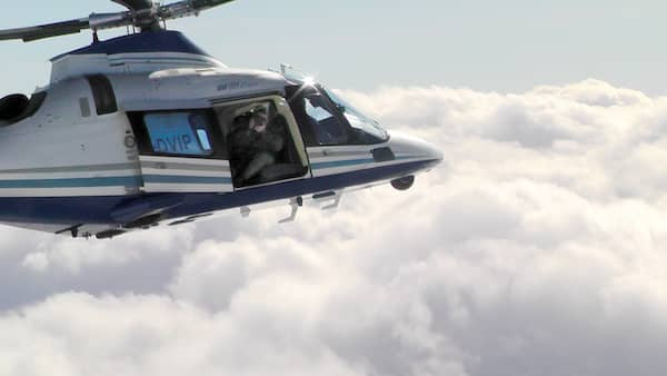 Ein Mann filmt aus der offenen Tür eines fliegenden Hubschraubers.