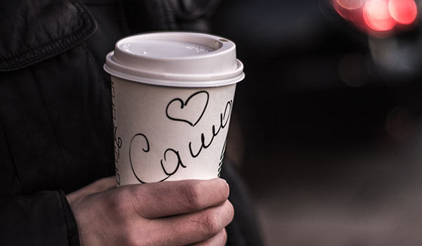 Eine Person mit einem Kaffeebecher, auf dem ihr Name steht.
