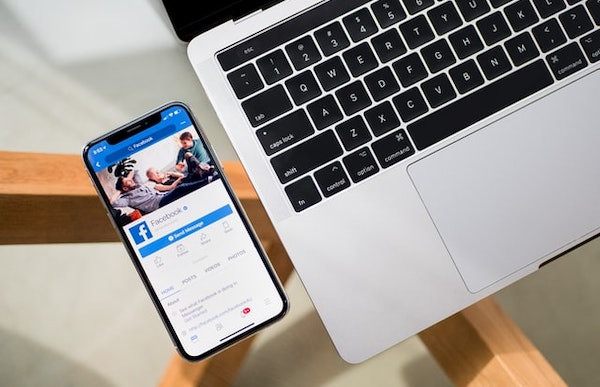 Ein Smartphone mit geöffneter Facebook-App liegt neben einem Laptop.