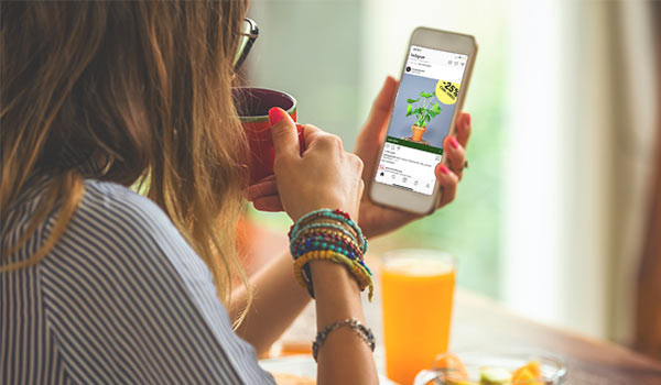 Eine Frau trinkt Kaffee und schaut sich auf ihrem Handy eine Anzeige für Zimmerpflanzen auf Instagram an.