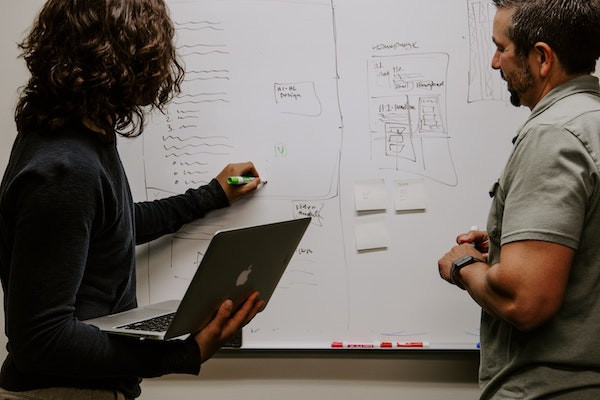 Ein Mann und eine Frau planen eine E-Mail-Strategie an einem Whiteboard, ohne die man keinen E-Mail-Verteiler erstellen kann.