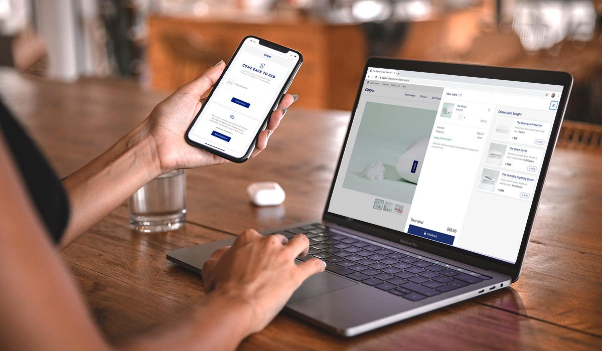 Eine Frau hält ein Telefon, auf dem eine verlassener-Warenkorb-E-Mail angezeigt wird, die sie zu ihrem Warenkorb im Webshop von Casper zurückführt.