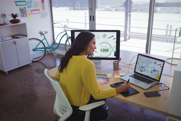 Ein Designer bearbeitet mit Laptop und Computer Bilder, die er in Adobe Illustrator benutzen kann.