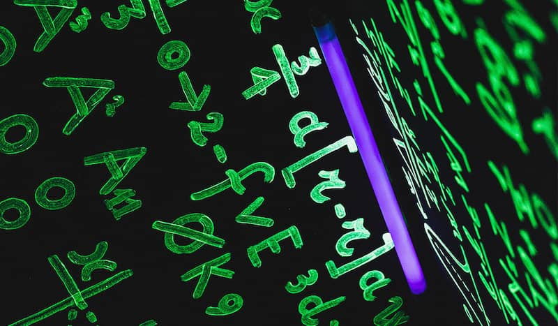 Mathematische Formeln wurden mit fluoreszierender Farbe an eine Tafel geschrieben und leuchten unter einem Schwarzlicht auf.