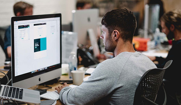 Ein Mann sitzt im Büro an einem Computer und entwirft eine E-Mail für kostenloses E-Mail-Marketing.