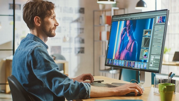 Ein Grafikdesigner sitzt am Schreibtisch und arbeitet an einem Computer, weil er JPG in PSD konvertieren möchte.