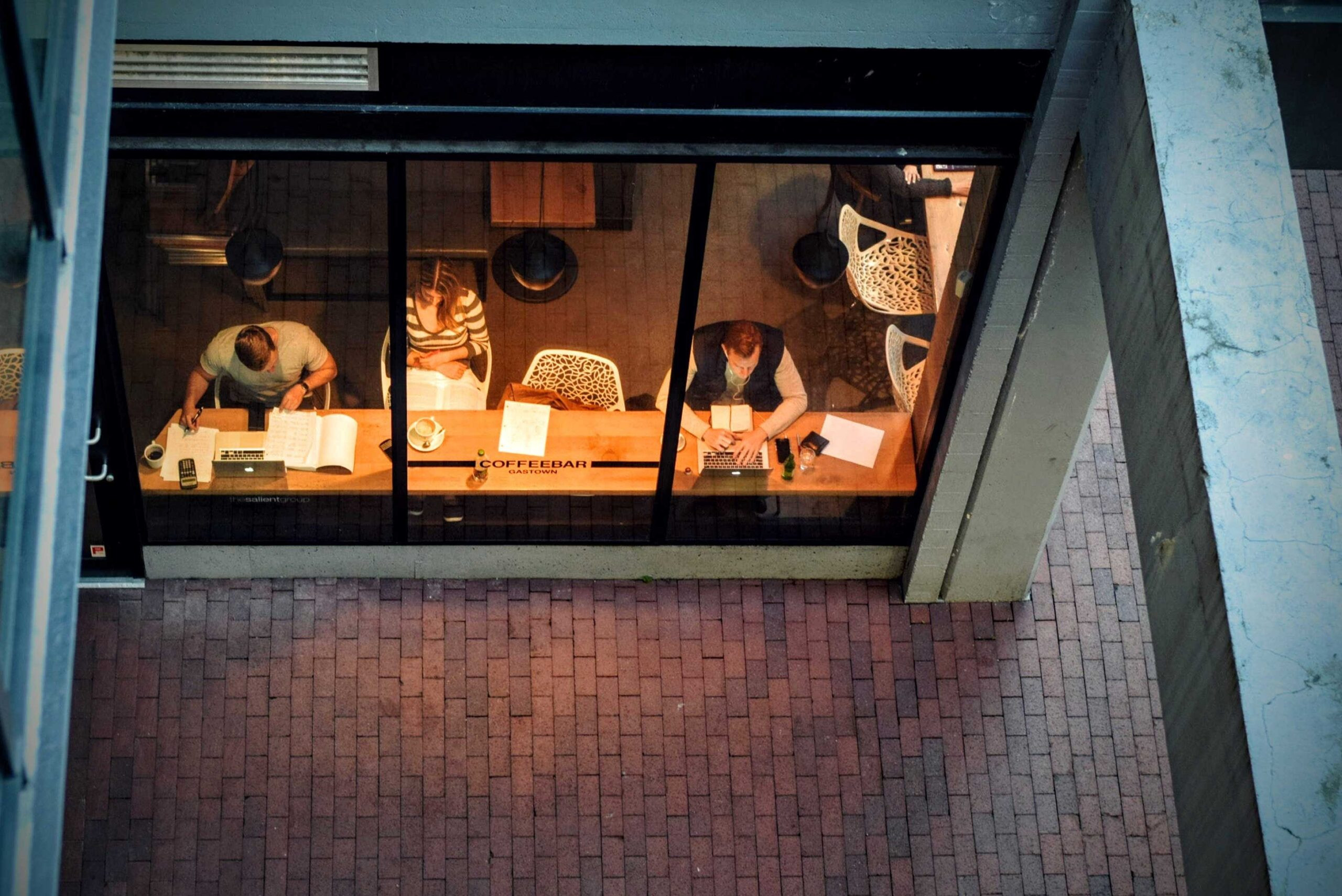 Birds eye view of a building with large windows and dim lights with several people working at a large table by the windows