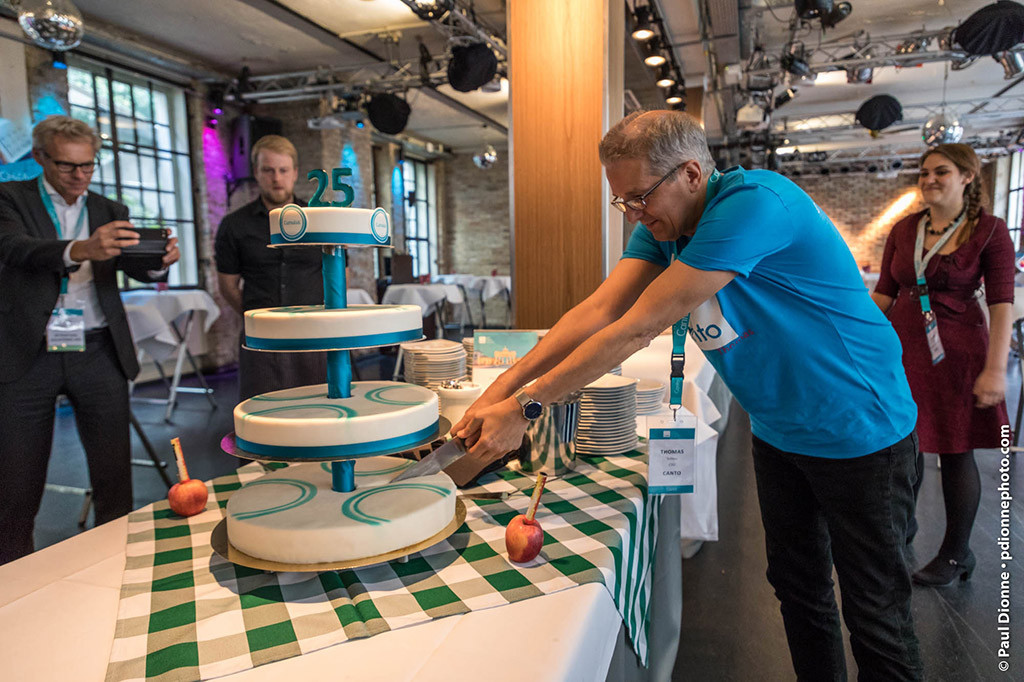 Picture of a man cutting a cake, while other persons look on and take pictures.