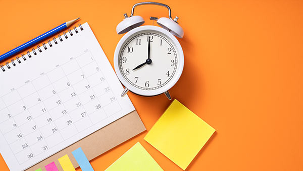 An alarm clock on a desk with a calendar.