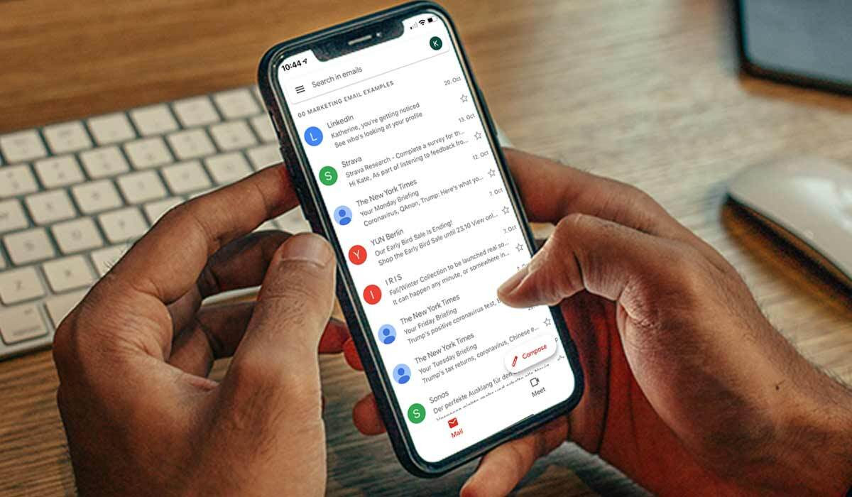 Hands holding a smartphone with an email inbox on the screen.