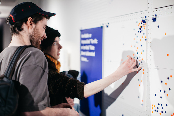 two people looking at orange and blue scatter point graphs going up and to the right over a burred white board