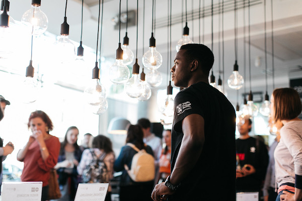An image of a young man looking at low hanging light bulbs, over a blurred background with groupd of people looking at the same structure.