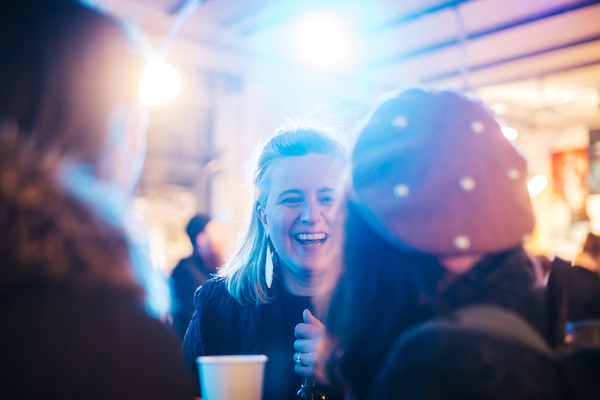 An image of some woman chatting with each other in a social setting with blue lights above an otherwise casually lit room