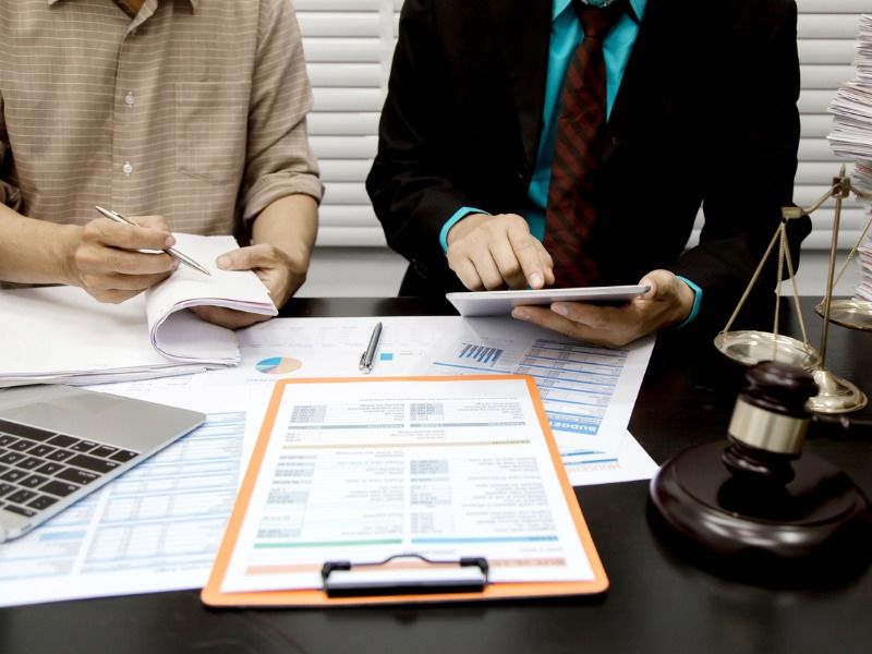 Two people sit at a table and consult on a document, on the table is a scale.