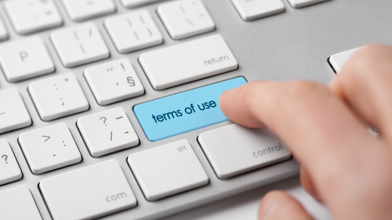 A computer keyboard on which a hand presses a highlighted key for terms of use.