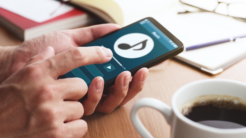 A man holding a smartphone with a music playlist on the screen.